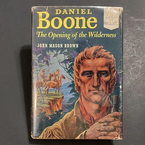 May include: A vintage book cover with a portrait of Daniel Boone, a famous American frontiersman. The title is "Daniel Boone: The Opening of the Wilderness" by John Mason Brown. The cover features a colorful illustration of Boone in a forest setting.