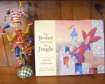 Op de afbeelding: Een kinderboek getiteld "The Jester Has Lost His Jingle" van David Saltzman met een nawoord van Maurice Sendak. De omslag toont een illustratie van een nar in een rood en blauw kostuum dat op een kasteelmuur staat.