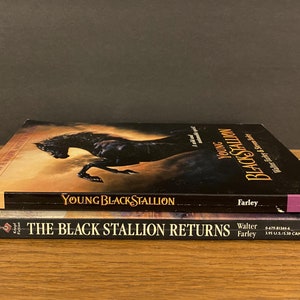 Pu&ograve; includere: Due libri tascabili impilati uno sopra l'altro. Il libro in alto &egrave; "Young Black Stallion" di Walter Farley. Il libro in basso &egrave; "The Black Stallion Returns" di Walter Farley.