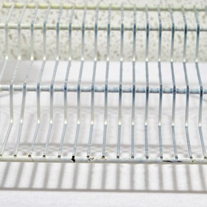 May include: White metal wire rack with two tiers. The rack is designed to hold items like dishes or other kitchen items.