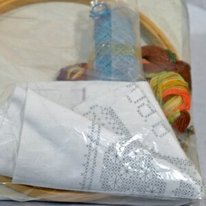 Puede incluir: Un kit de bordado de punto de cruz con una tela blanca, un aro de bordado de madera y hilo de bordar de colores.