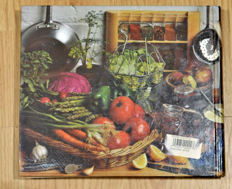 May include: A still life image of a variety of fresh vegetables, including red cabbage, green peppers, asparagus, carrots, and onions. The vegetables are arranged in a wicker basket with a white garlic bulb and a few green sprigs of herbs. There are also jars of preserved food and a metal colander filled with lettuce in the background.