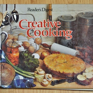 May include: A vintage cookbook titled "Reader's Digest Creative Cooking" with a colourful cover featuring a pie, eggs, vegetables, and a rolling pin.