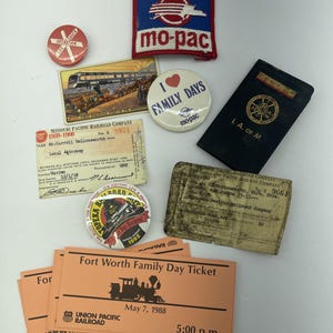 May include: A collection of vintage railroad memorabilia, including patches, pins, tickets, and a small book. The items feature logos and text related to the Missouri Pacific Railroad, Union Pacific Railroad, and family day events. The items are in various colors.