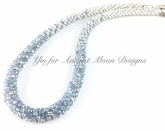 May include: A light blue beaded necklace with silver accents. The necklace is made of small, round beads and has a clasp closure. The text "Yin for Ancient Moon Designs" is visible in the image.