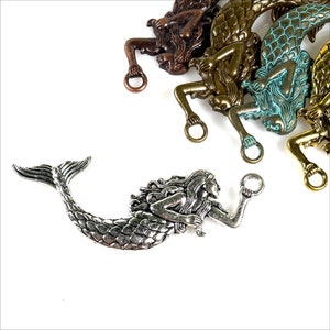 May include: A collection of mermaid charms in various metallic finishes, including silver, bronze, and gold. Each charm features a detailed mermaid design with a loop for attaching to jewelry or other crafts. The mermaids are lying down with their arms raised.