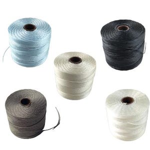 以下が含まれることがあります： ライトブルー、ブラック、ホワイト、グレー、オフホワイトの5色の紐の巻き。各巻きは円筒形で、濃い茶色の芯があります。紐はきつく巻かれており、一部の巻きからは紐が出ています。