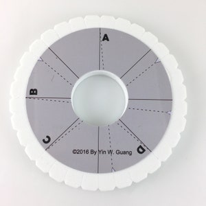 May include: A circular grey braiding disc with a white scalloped edge. The disc has a central hole and is divided into sections labelled A, B, C, and D. The text "©2016 By Yin W. Guang" is printed on the disc.