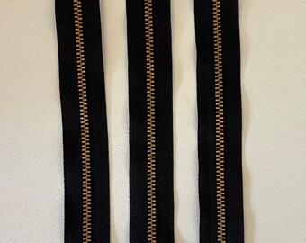 May include: Three black zipper closures with gold metal teeth. The zippers are approximately 10 inches long.