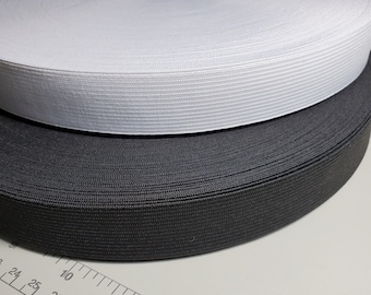 May include: Two rolls of elastic, one black and one white, are stacked on top of each other. A ruler is visible in the bottom of the image.