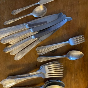 Könnte beinhalten: Ein Set antiken Bestecks, bestehend aus Messern, Gabeln und Löffeln. Das Besteck ist aus Silber und hat ein florales Design. Das Besteck ist auf einer Holzoberfläche angeordnet.