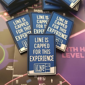 May include: Blue and white patch with the text "Line is capped for this experience" and the logo "Line Con" in white letters on a blue background. The patch is surrounded by a black border.