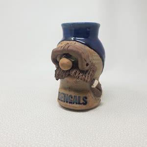 May include: A ceramic vase with a gnome-like face design. The top is dark blue, the face is tan and brown, and the beard is textured. The word "BENGALS" is written in blue on the base. A unique decorative item.
