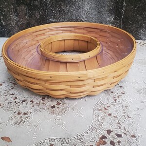 Peut inclure: Un panier rond en copeaux de bois brun clair tressé, doté d'un large bord extérieur et d'un compartiment circulaire central plus petit et surélevé. Le panier comprend un insert en plastique transparent qui tapisse l'intérieur, formant un plat.