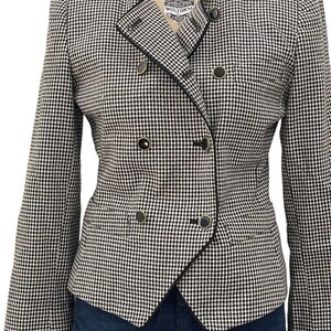 May include: A black and white houndstooth blazer with a double-breasted closure and black trim. The blazer has a slightly asymmetrical design and features gold-toned buttons.