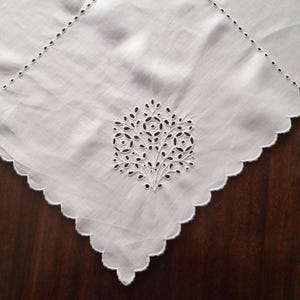 May include: White handkerchief with a decorative embroidered tree design. The handkerchief has a scalloped edge and small embroidered details along the border. The tree design is in the center of the handkerchief.