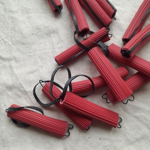 Peut inclure: Un ensemble de rouleaux à cheveux rouges avec des élastiques noirs. Les rouleaux sont faits d'un matériau flexible et ont une texture côtelée.