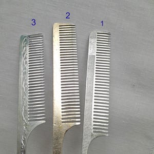 May include: Three silver combs with different designs. The comb labeled "1" has a plain design, the comb labeled "2" has a slightly textured design, and the comb labeled "3" has a decorative floral design.