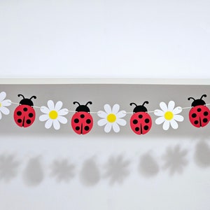 May include: A red and black ladybug garland with white daisy flowers. The garland is strung with white thread and is perfect for a spring or summer party.