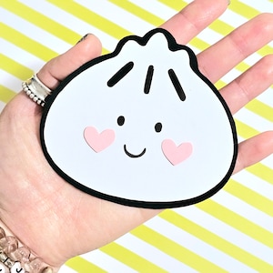 May include: A white and black cartoon dumpling with a smiling face and pink hearts on its cheeks.