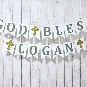 May include: White banner with green letters spelling "God Bless Logan" with gold glitter crosses between each word.