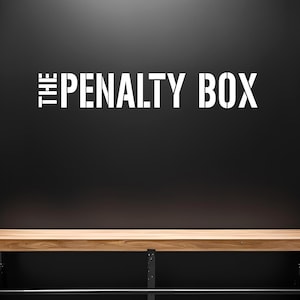 Puede incluir: Un banco de madera con patas de metal negro y una barra de metal negro debajo. El banco está frente a una pared negra con las palabras "THE PENALTY BOX" escritas en blanco.