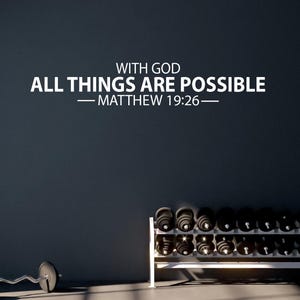Puede incluir: Una pared oscura con el texto blanco "WITH GOD ALL THINGS ARE POSSIBLE - MATTHEW 19:26". Un estante de pesas contiene múltiples mancuernas negras. Una barra con pesas descansa en el suelo.