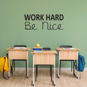 May include: Three wooden desks with black chairs and backpacks in a classroom setting. The wall is green and has the text "WORK HARD Be Nice" written on it.
