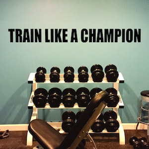 May include: A home gym with a weight rack, a weight bench, and a stool. The wall has a motivational quote that reads "TRAIN LIKE A CHAMPION".