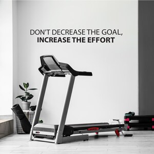May include: A black and silver treadmill with the motivational quote "Don't decrease the goal, increase the effort" on a white wall behind it.