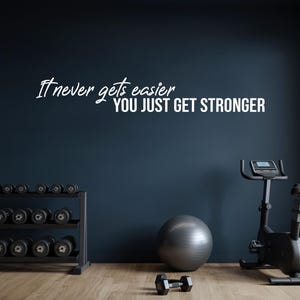 May include: A home gym with a stationary bike, dumbbells, a weight rack, and a motivational quote on the wall that reads "It never gets easier, you just get stronger."