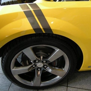 May include: A yellow car with black racing stripes on the wing. The car has a silver rim with five spokes and a black tyre.