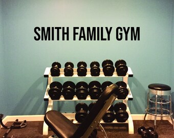 May include: A home gym with a weight rack, a weight bench, and a stool. The wall is painted a light blue colour and has the words "SMITH FAMILY GYM" written in black letters.
