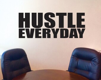Può includere: Adesivo da parete in bianco e nero con il testo "Hustle Everyday" in grassetto. L'adesivo è esposto su una parete bianca sopra un tavolo di legno con due sedie in pelle nera.