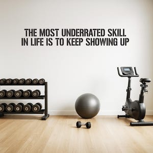 Könnte beinhalten: Ein Heim-Fitnessstudio mit einem motivierenden Zitat an der Wand. Die Szene umfasst ein Hantelregal mit Gewichten, einen Gymnastikball, ein stationäres Fahrrad und eine einzelne Hantel auf einem Holzboden.