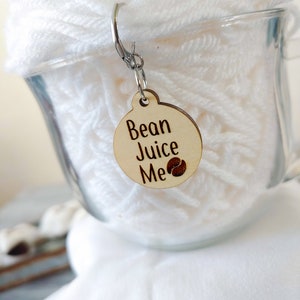 May include: A wooden tag with a coffee bean design and the text "Bean Juice Me" attached to a skein of white yarn.