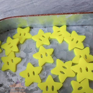 May include: A collection of yellow star-shaped buttons with two holes in each star. The buttons are in a metal container.