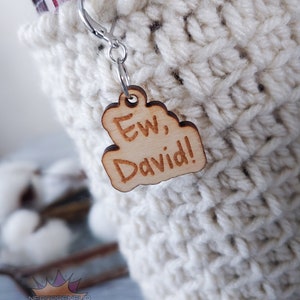 May include: A white crocheted cup cozy with a wooden tag that says "Ew, David!" hanging from it.