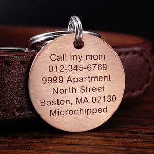 Puede incluir: Chapa de identificaci&oacute;n para perro de cobre con texto grabado: "Call my mom 012-345-6789 9999 Apartment North Street Boston, MA 02130 Microchipped"