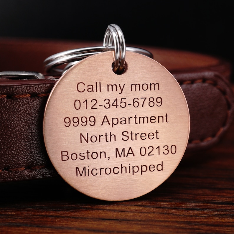 Puede incluir: Chapa de identificaci&oacute;n para perro de cobre con texto grabado: "Call my mom 012-345-6789 9999 Apartment North Street Boston, MA 02130 Microchipped"