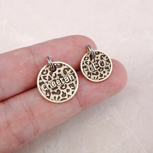 May include: Two gold-toned pet ID tags with a leopard print design. One tag says "Cheetah" and the other says "Leo".