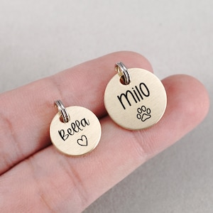 Peut inclure: Deux m&eacute;dailles d'identification rondes pour animaux de compagnie de couleur or avec des noms grav&eacute;s. La m&eacute;daille de gauche indique "Bella" avec un symbole de c&oelig;ur. La m&eacute;daille de droite indique "Milo" avec un symbole de patte.
