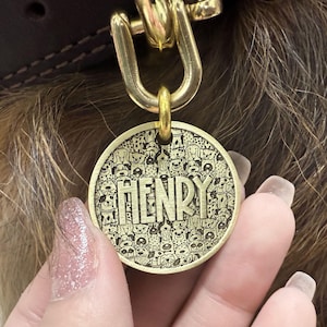 Puede incluir: Chapa de perro de lat&oacute;n con un dise&ntilde;o de muchos perros y el nombre "HENRY" grabado en ella.