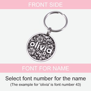 Puede incluir: Llavero de plata con una etiqueta redonda con un dise&ntilde;o floral y el nombre "olivia" en letras blancas. La etiqueta est&aacute; unida a un llavero de plata.
