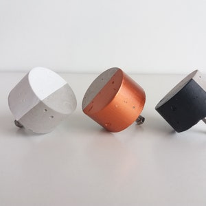 May include: Three concrete cabinet knobs with a split design. The knobs are painted white, copper, and black.
