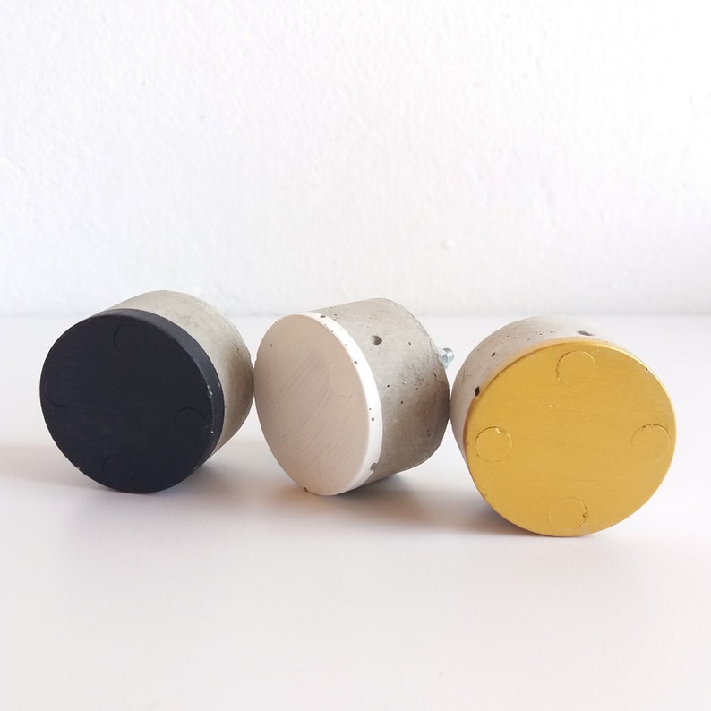 Peut inclure: Trois boutons ronds en b&eacute;ton avec diff&eacute;rentes finitions de couleur. Les boutons sont noirs, blancs et dor&eacute;s.