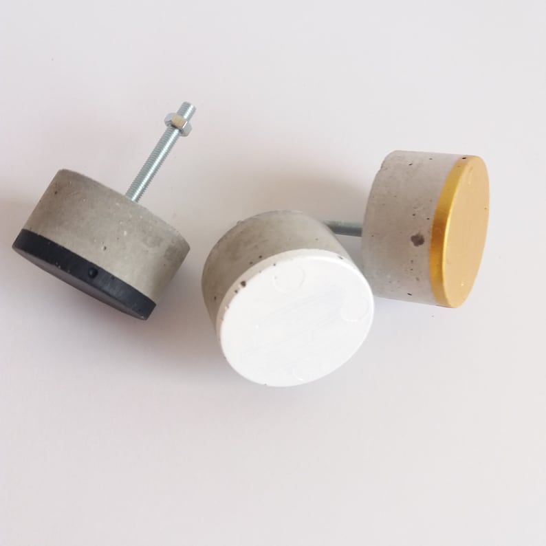 Peut inclure: Trois boutons de porte en b&eacute;ton avec diff&eacute;rentes finitions. Un bouton est peint en blanc, un autre en or et le dernier en noir.