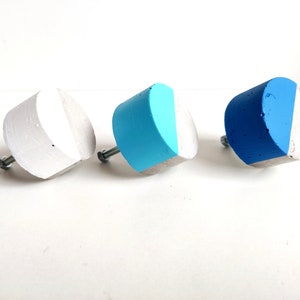 May include: Three concrete cabinet knobs with a half-circle design. The knobs are painted in shades of blue and white.