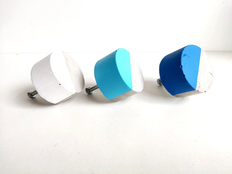 May include: Three concrete cabinet knobs with a half-circle design. The knobs are painted in shades of blue and white.