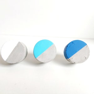 May include: Three round concrete knobs with a half-circle of paint on each. The knobs are painted white, light blue, and dark blue.